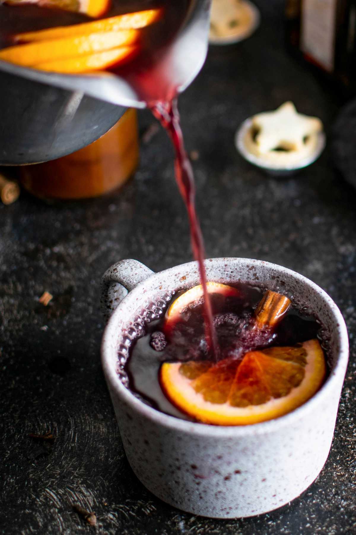 pouring Gluhwein in a mug filled with spices and citrus